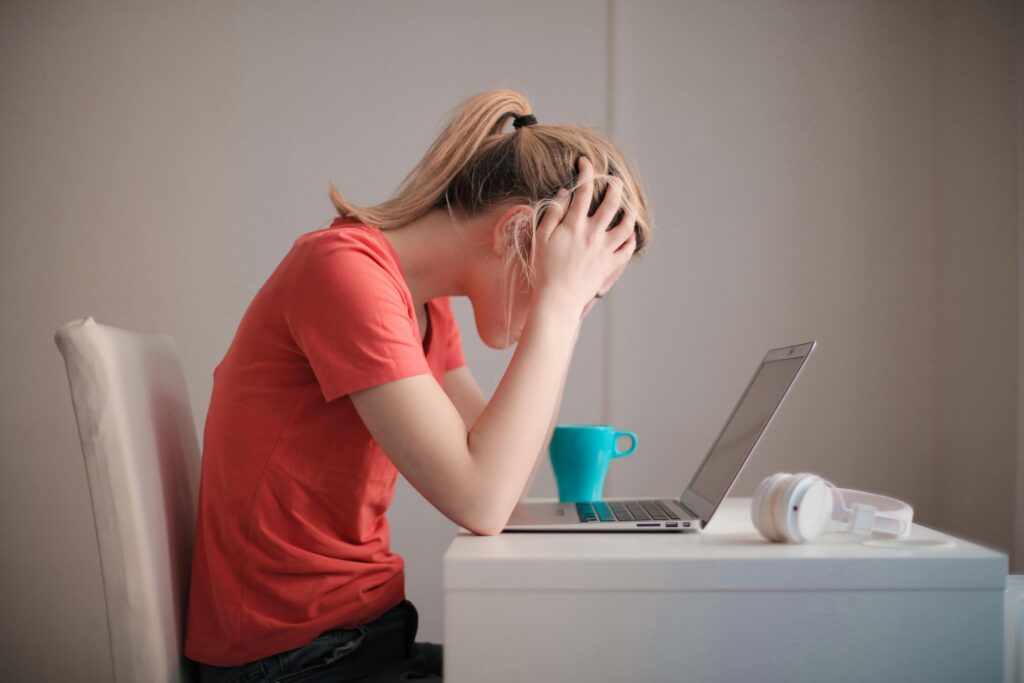 Woman sitting at a desk slouched over her laptop with her hands on her head. She appears to be frustrated.