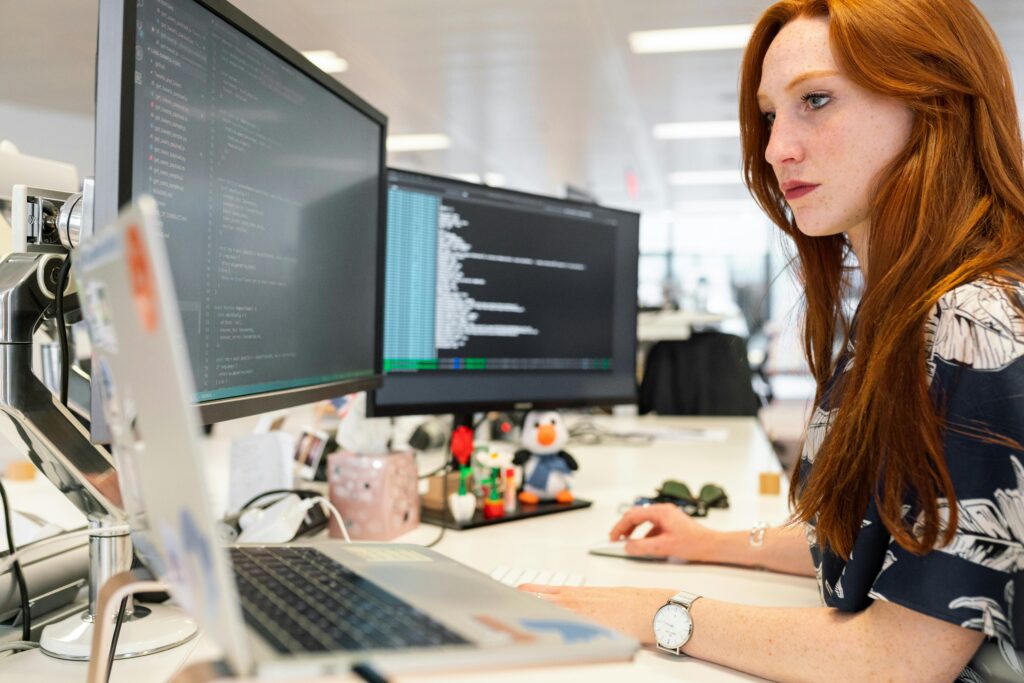 Woman sitting at desk with multiple monitors that appear to have a code editor on the screen