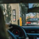 view from the drivers seat of a car in a drive through. a car sits in front of them at the pay window